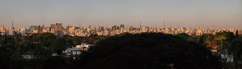 Jardins de São Paulo ao entardecer, com as torres da Avenida Paulista ao fundo.